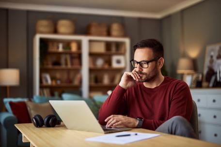 Mann arbeitet konzentriert am Laptop im Wohnzimmer